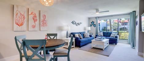 A modern living room with a dining area, featuring a round table, blue chairs, a blue sofa, and artwork on the walls.