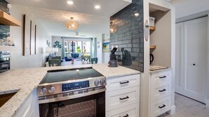 A modern kitchen with a built-in stove, white cabinetry, and a dining area in the background. - Miracle's Runaway Bay 117 by SeaBreeze Vacation (Bradenton Beach)