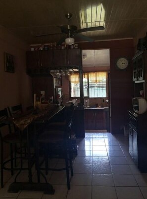 A compact kitchen area with a dining table and chairs, featuring a ceiling fan and a window with curtains.