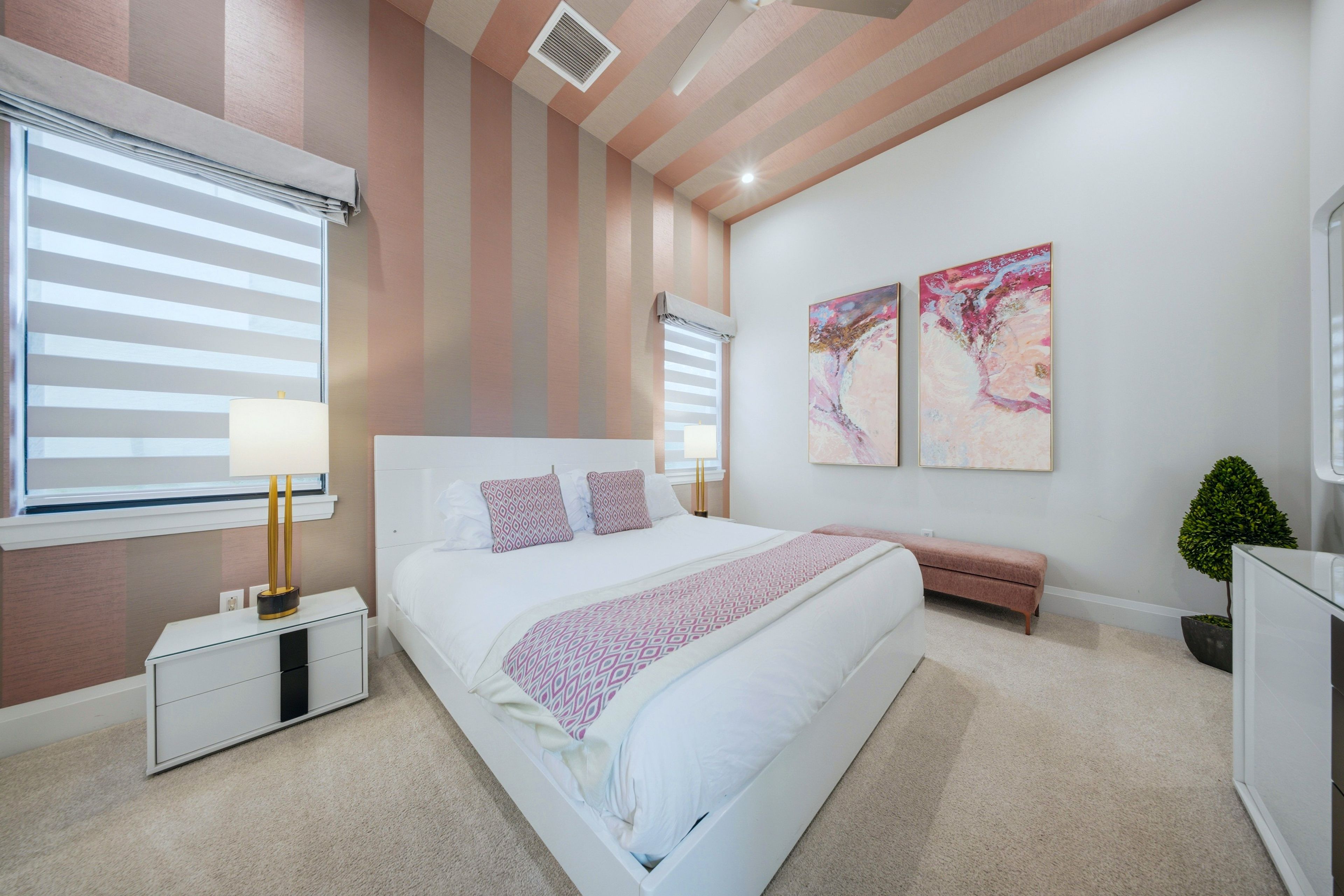 A modern bedroom with a large bed, bedside tables, a bench, and two abstract paintings.