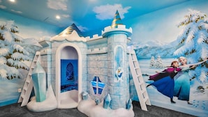 A play area with a castle-themed play structure, a mural with snow-covered trees, and a character from a popular movie.