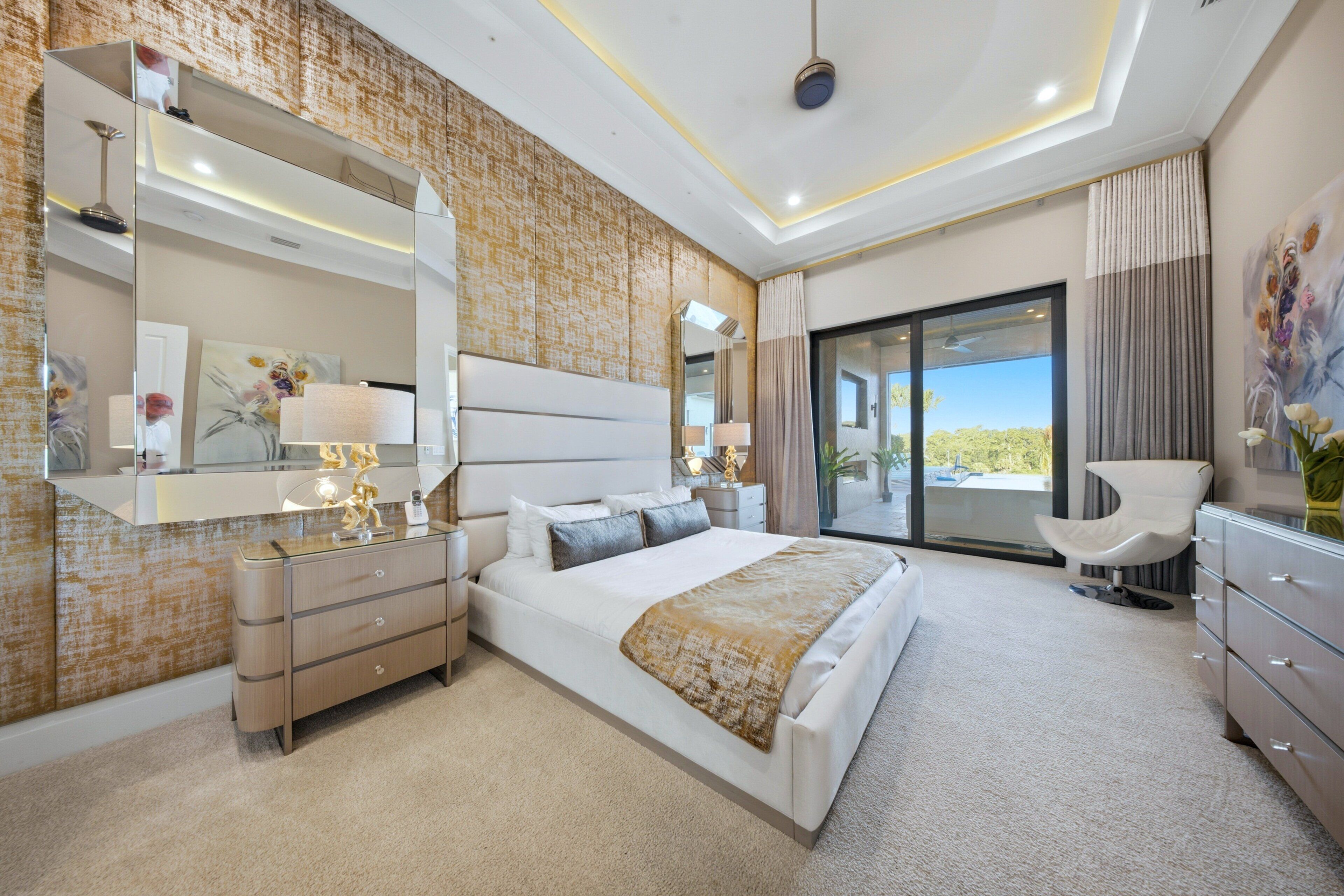 A modern bedroom with a large bed, a walk-in closet, a bathroom with a mirror, and a view through a glass door.