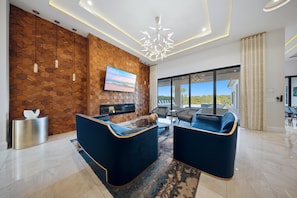 A modern living room with a wooden wall, a flat-screen TV, and a large window offering a view of the outdoors.