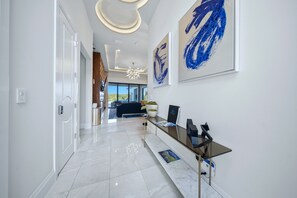 A modern hallway with a glass reception desk, framed artwork, and a chandelier. - Reunion Mansion with Infinity Pool & Game Room (Kissimmee)