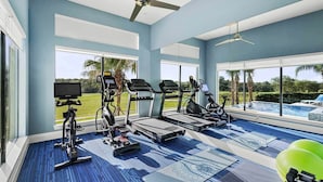 A gym with exercise equipment, large windows, and a view of a swimming pool.