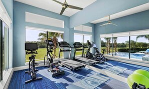 A gym with exercise equipment, large windows, and a view of a swimming pool. - Luxurious Mansion with Infinity Pool at Reunion (Kissimmee)