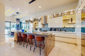 A modern kitchen with a central island, bar stools, and a backsplash with blue tiles. - Luxurious Mansion with Infinity Pool at Reunion (Kissimmee)
