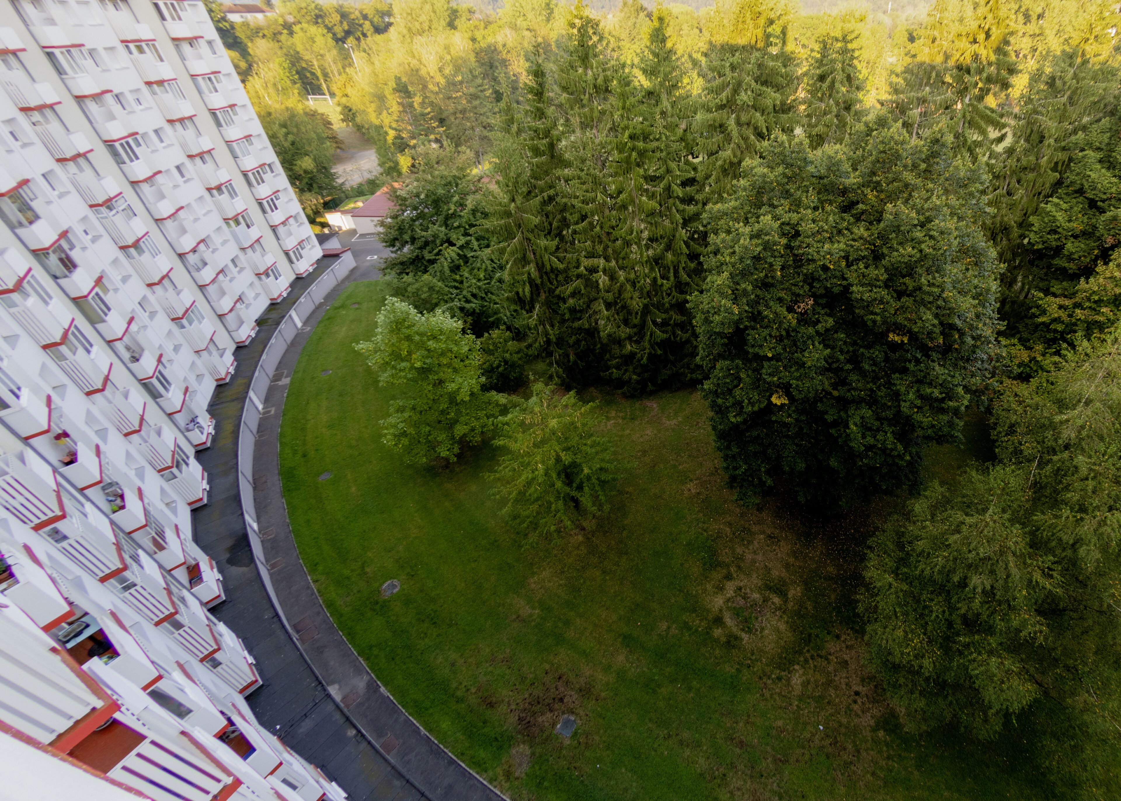 Een hoog gebouw met meerdere balkons, een gebogen weg en een dichtbegroeid groen gebied met bomen.
