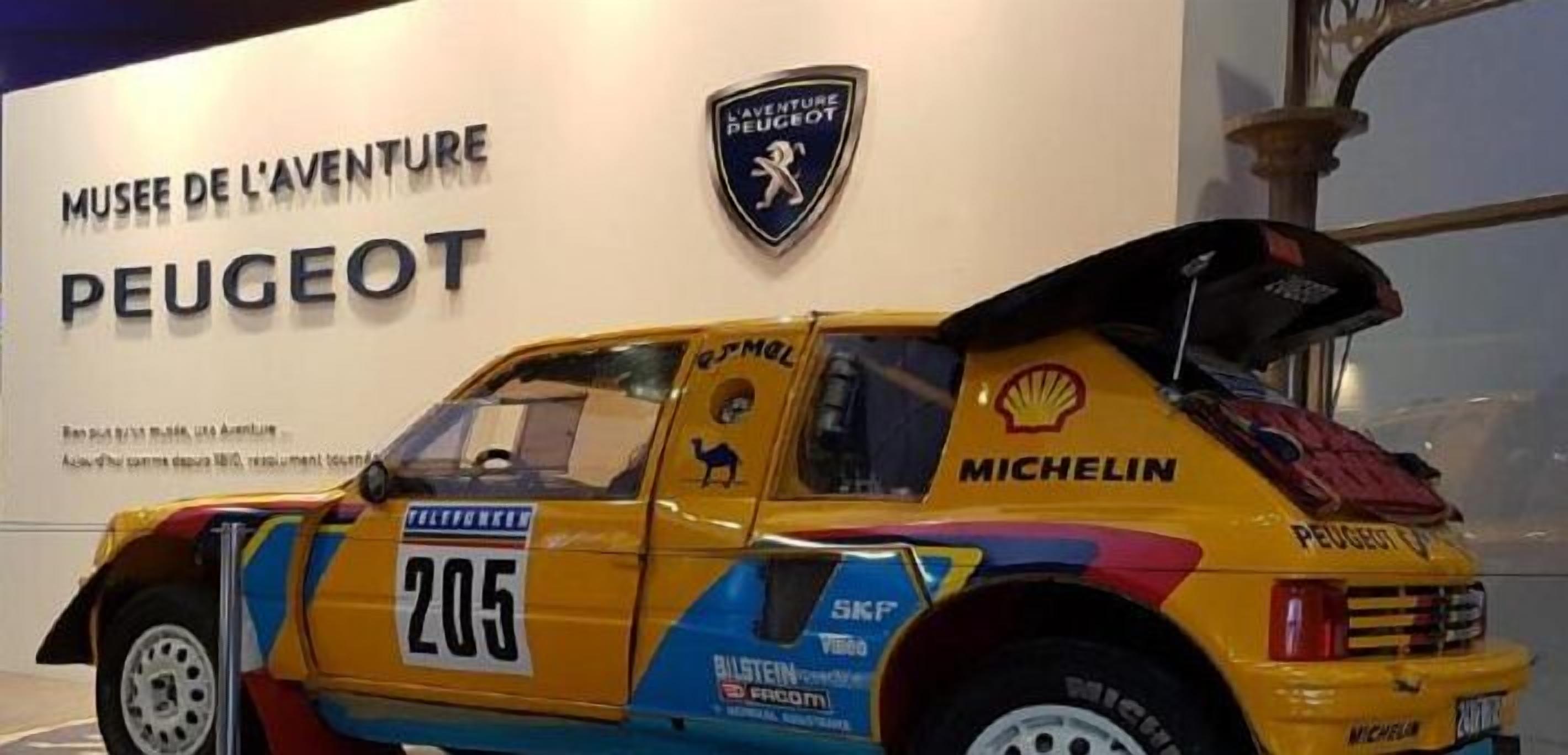 Un'auto da rally gialla con la scritta Peugeot, numero 205, parcheggiata davanti al museo Peugeot.