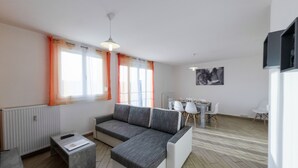 Una sala de estar moderna con un sofá seccional gris, una mesita de centro pequeña y un comedor con una mesa y sillas blancas.