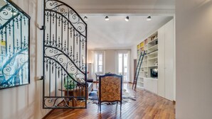 A spacious hallway with wooden flooring, a decorative metal gate, a patterned chair, and white shelving units. - GuestHost - Wonderful 75 sqm apartment, located on the second floor of a building without a lift, perfect for 4 people.The property is in the heart of the historic center, close to the Sant'Orsola Malpighi Hospital and the main services (train and bus st (Bologna)