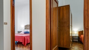 A hallway leading to a bedroom with a wooden wardrobe and a bed with a red bedspread. - GuestHost - Wonderful 75 sqm apartment, located on the second floor of a building without a lift, perfect for 4 people.The property is in the heart of the historic center, close to the Sant'Orsola Malpighi Hospital and the main services (train and bus st (Bologna)