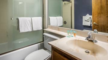 A bathroom with a glass-enclosed shower, a white toilet, a sink with toiletries, and a mirror.
