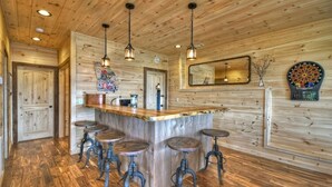 Une cuisine rustique aux murs en bois, avec un îlot central doté de tabourets, des luminaires suspendus et un jeu de fléchettes.