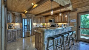 Une cuisine rustique avec des meubles en bois, un grand îlot central doté de tabourets, des appareils électroménagers en acier inoxydable et des luminaires suspendus.
