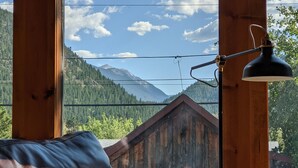 A wooden cabin with a leather couch and a lamp, overlooking a mountainous landscape.