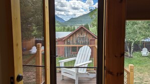 A wooden door with a glass panel leading to a deck with a white Adirondack chair and a wooden cabin in the background.