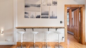 A bar area with four white stools, a wooden countertop, and a wall decorated with six framed pictures depicting natural landscapes.