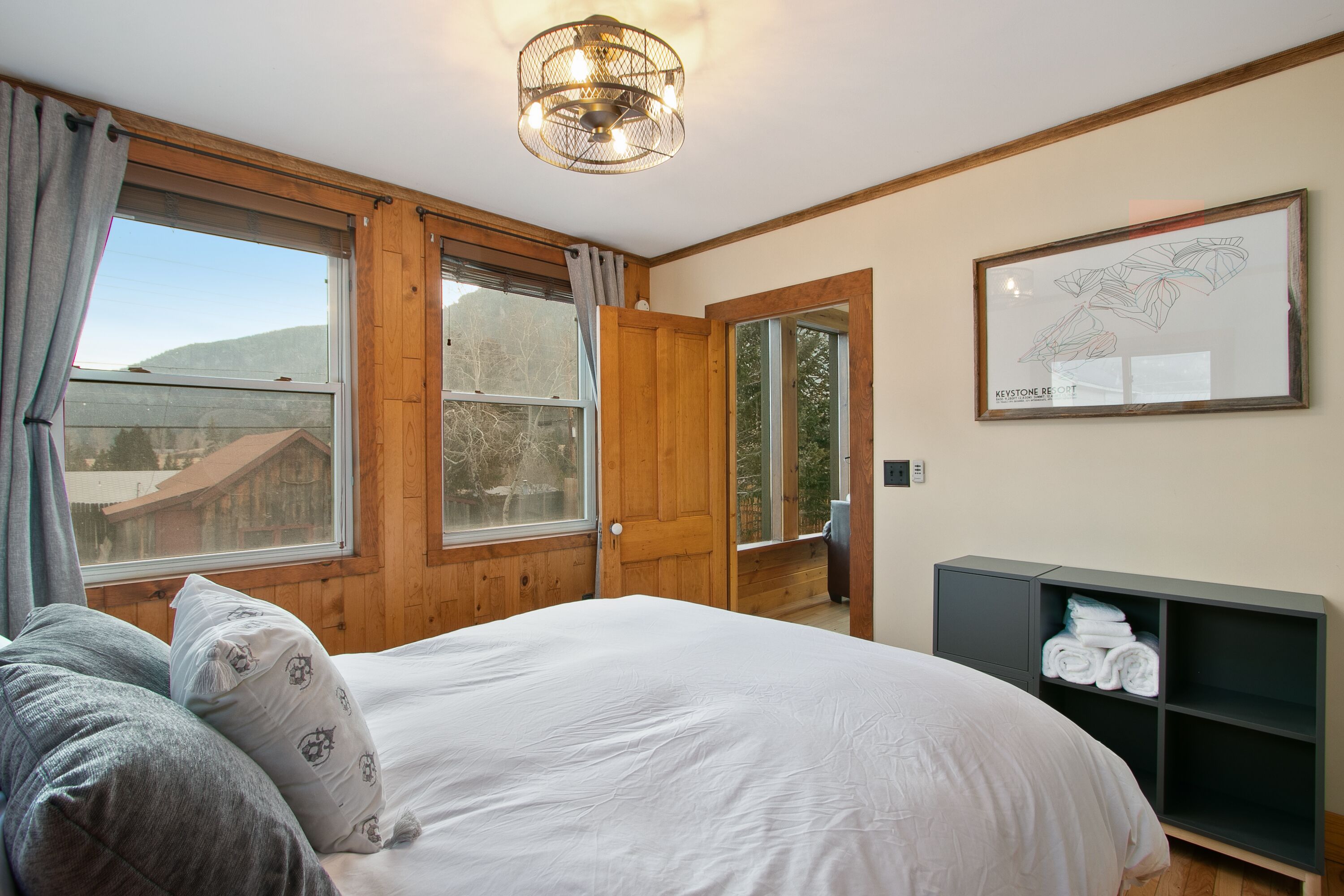 Une chambre avec un grand lit, des murs en bois, une porte en bois, une fenêtre donnant sur une montagne et une carte encadrée accrochée au mur.