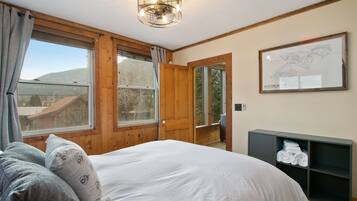 Une chambre avec un grand lit, des murs en bois, une porte en bois, une fenêtre donnant sur une montagne et une carte encadrée accrochée au mur.