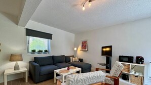 A modern living room with a sofa, a coffee table, a TV, and a small dining area. - CARNAC - Apartment 2 Rooms - 2/4 persons (CARNAC)