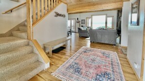 Un vaste espace de vie agrémenté d’un escalier en bois, d’un grand tapis et offrant une vue par les fenêtres.