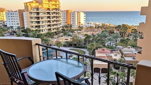 Un balcon avec une table ronde et des chaises donnant sur une zone de villégiature agrémentée de palmiers et d’une piscine.