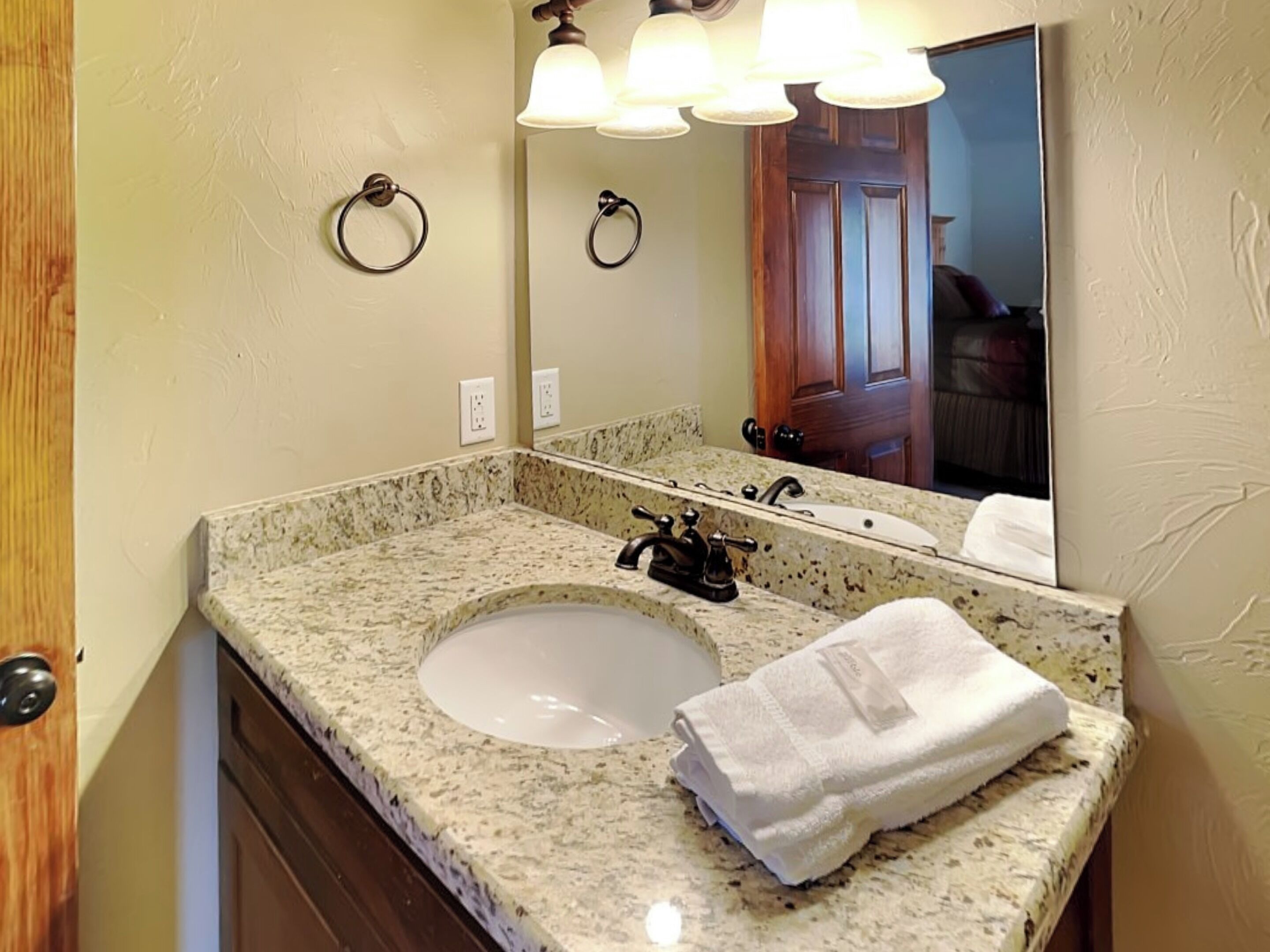 A bathroom with a granite countertop sink, a mirror, and a towel.