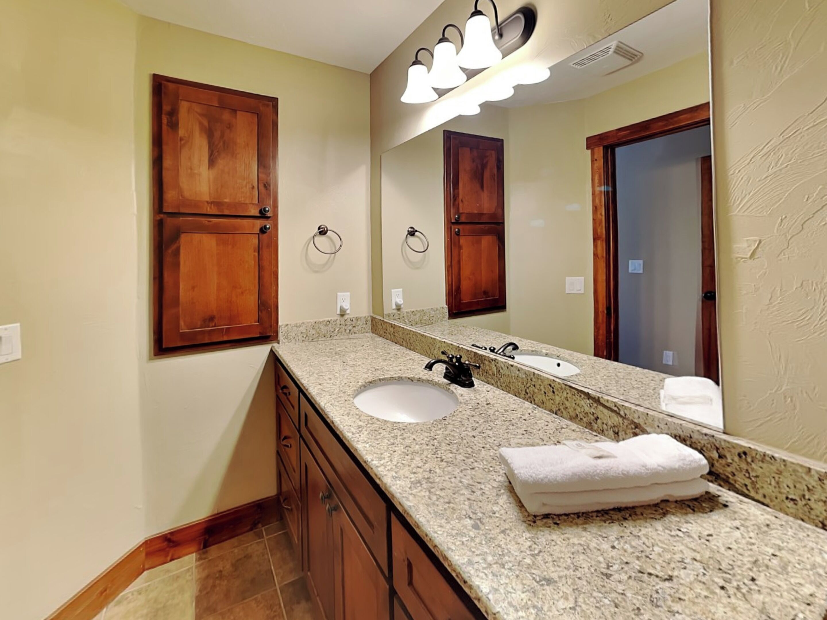 Une salle de bain avec un comptoir en granit, un lavabo, un miroir, des armoires en bois et une serviette posée sur le comptoir.