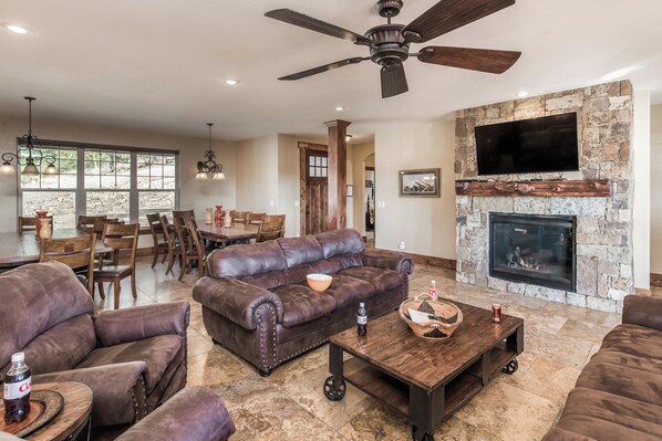 A spacious living room with leather sofas, a stone fireplace, and a ceiling fan. - Abbey Lodge by Ruidoso Vacation Rentals (Ruidoso)