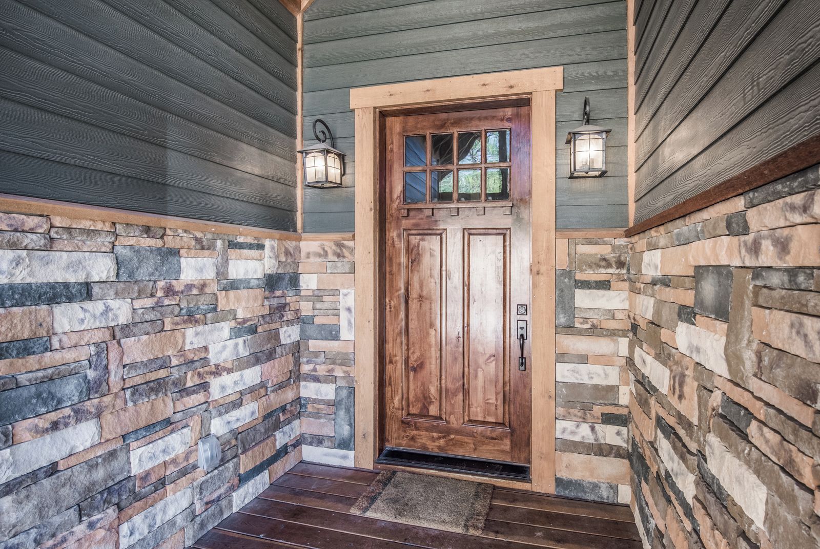 A wooden door with a stone wall on either side, a stone staircase leading up to it, and two wall-mounted lanterns.