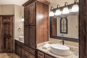 A bathroom with a wooden vanity, a large mirror, and a round sink. - Abbey Lodge by Ruidoso Vacation Rentals (Ruidoso)