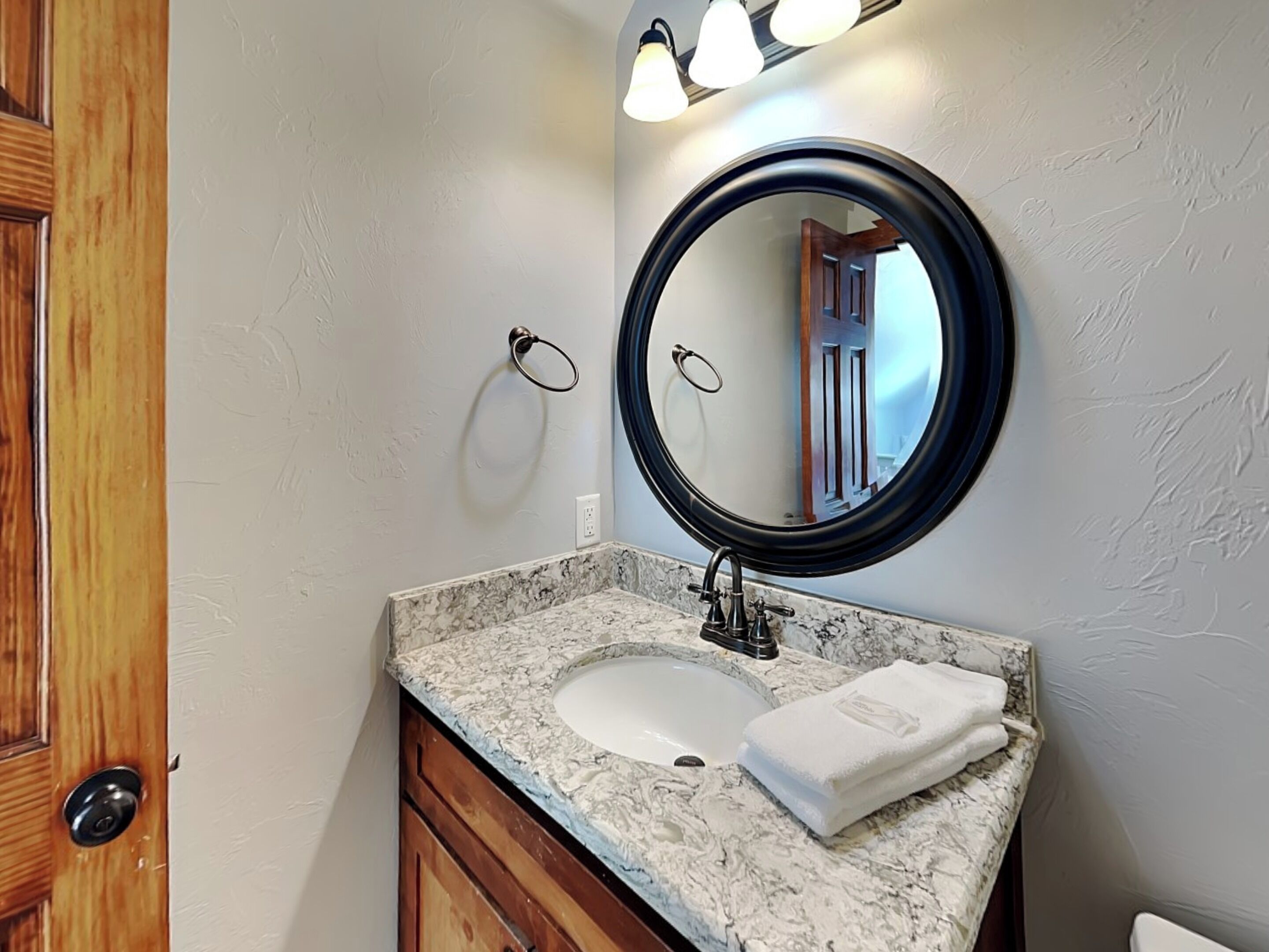 Une salle de bain avec un lavabo en marbre, un miroir rond et une serviette posée sur le comptoir.