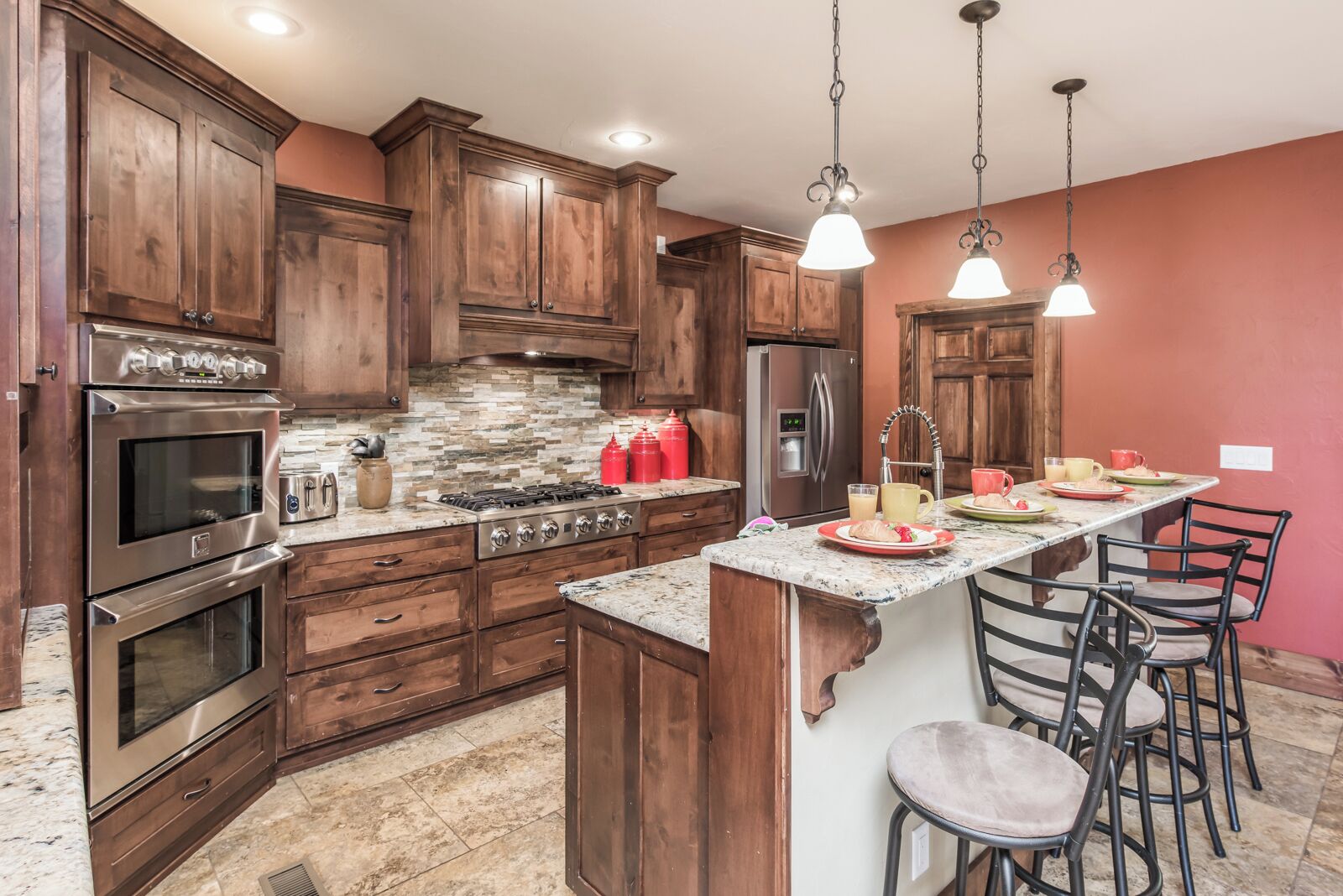 A kitchen with wooden cabinets, a stainless steel oven, a gas stove, a refrigerator, and a marble countertop.