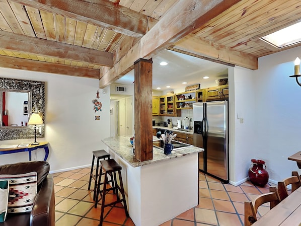 A kitchen with a central island, wooden ceiling beams, and a tiled floor. - Artist Road by Kokopelli Property Management (Santa Fe)