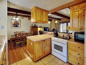 A kitchen with wooden cabinets, a stove, and a dining area with chairs.
