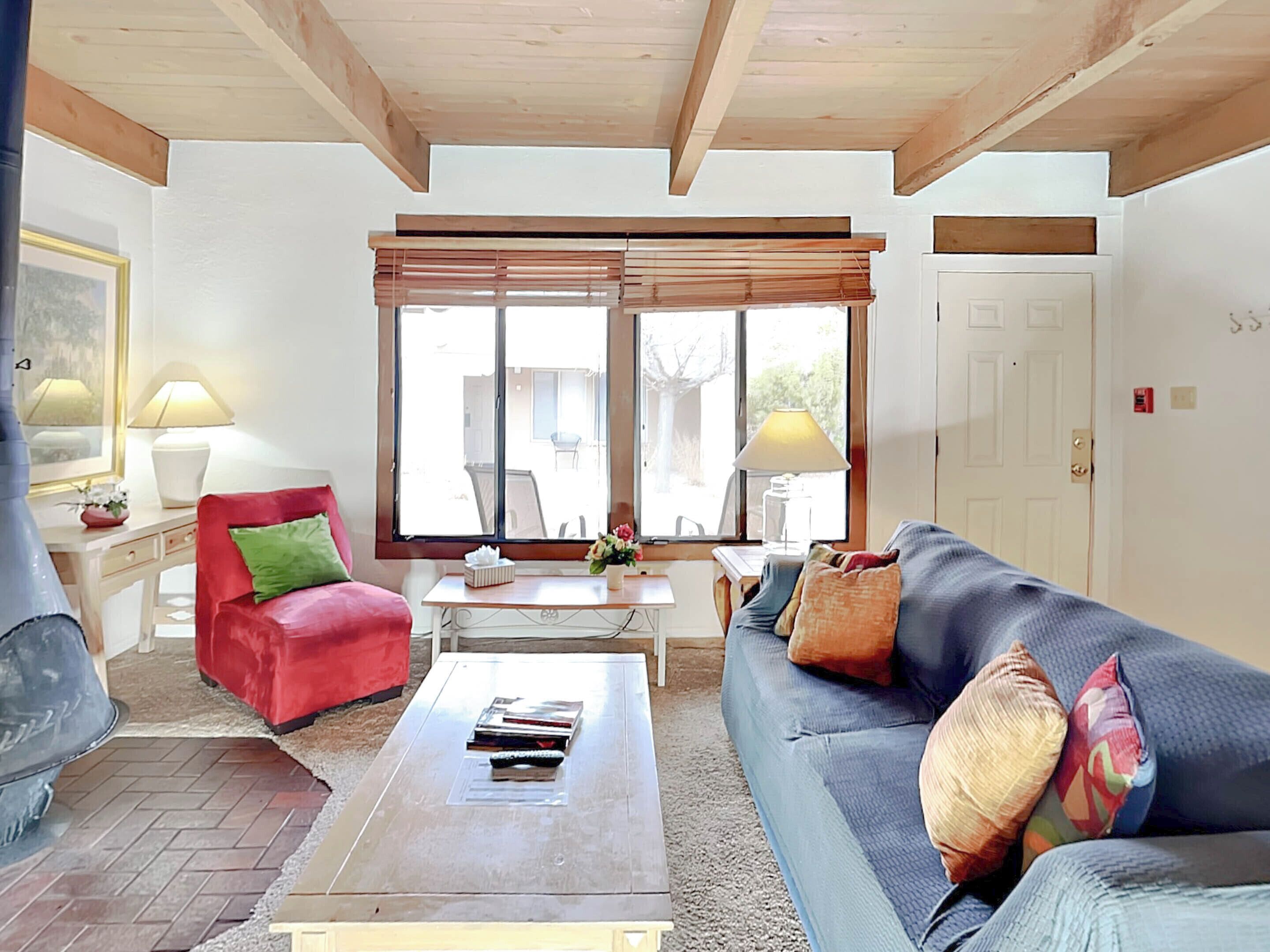 A living room with a red chair, a blue sofa, a coffee table, and a window with blinds.