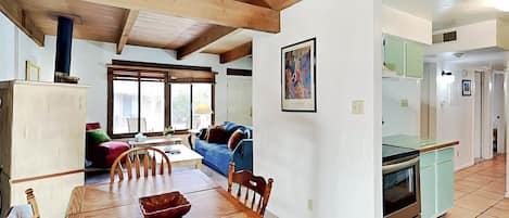 A spacious living room with a wooden dining table, blue sofa, and a kitchen area with a green countertop and oven.