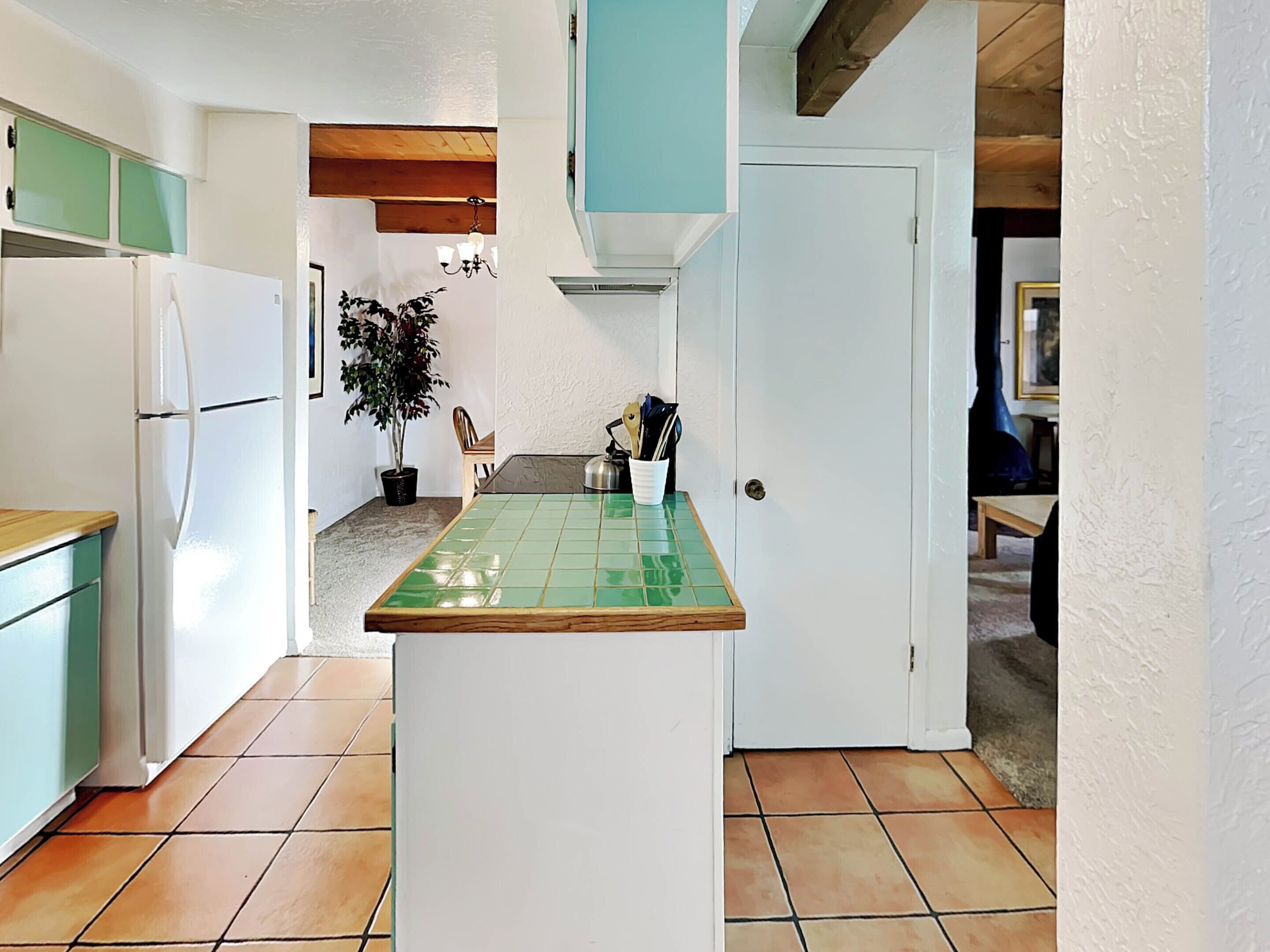 A narrow kitchen with a green-tiled island, white cabinets, and a potted plant.