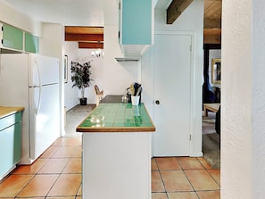 A narrow kitchen with a green-tiled island, white cabinets, and a potted plant. - Artist Road by Kokopelli Property Management (Santa Fe)