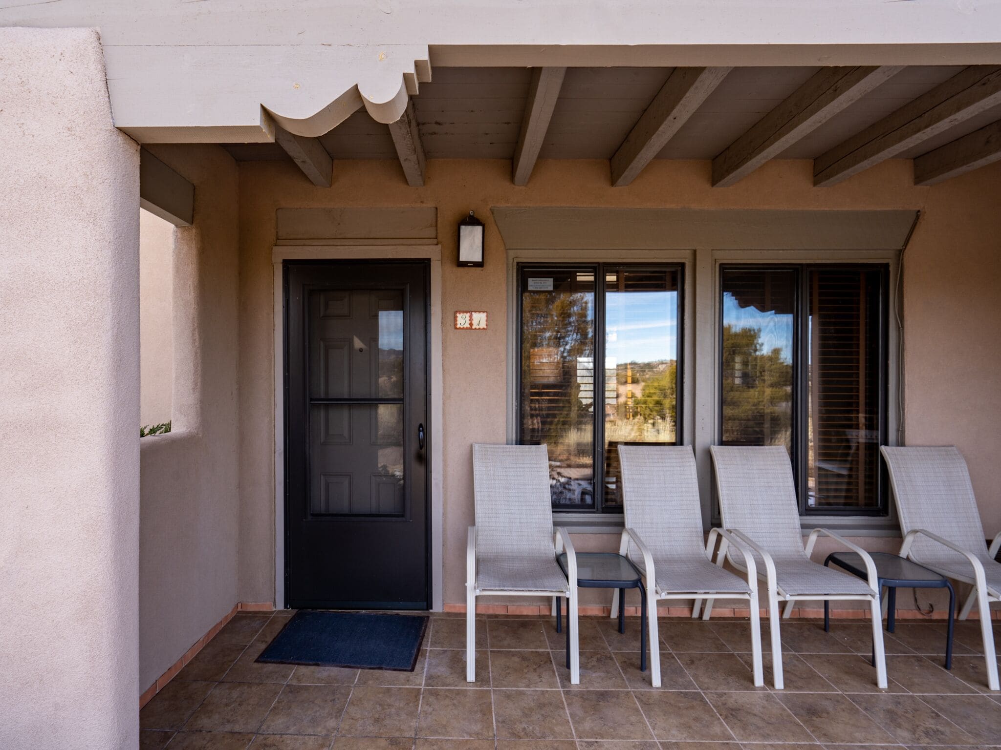 A covered patio with four lounge chairs, a black door, and a sliding glass door leading to a view.