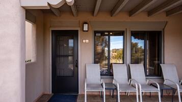 A covered patio with four lounge chairs, a black door, and a sliding glass door leading to a view.