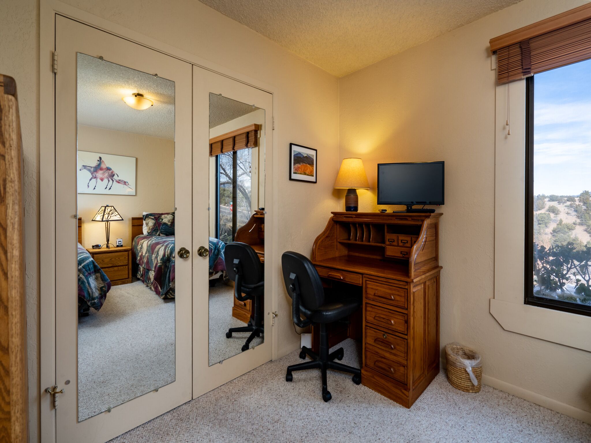 A bedroom with a desk, chair, and a bed with a colorful blanket.