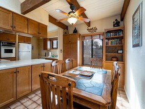 A kitchen with wooden cabinets, a built-in oven, a refrigerator, a dining table with chairs, and a ceiling fan.
