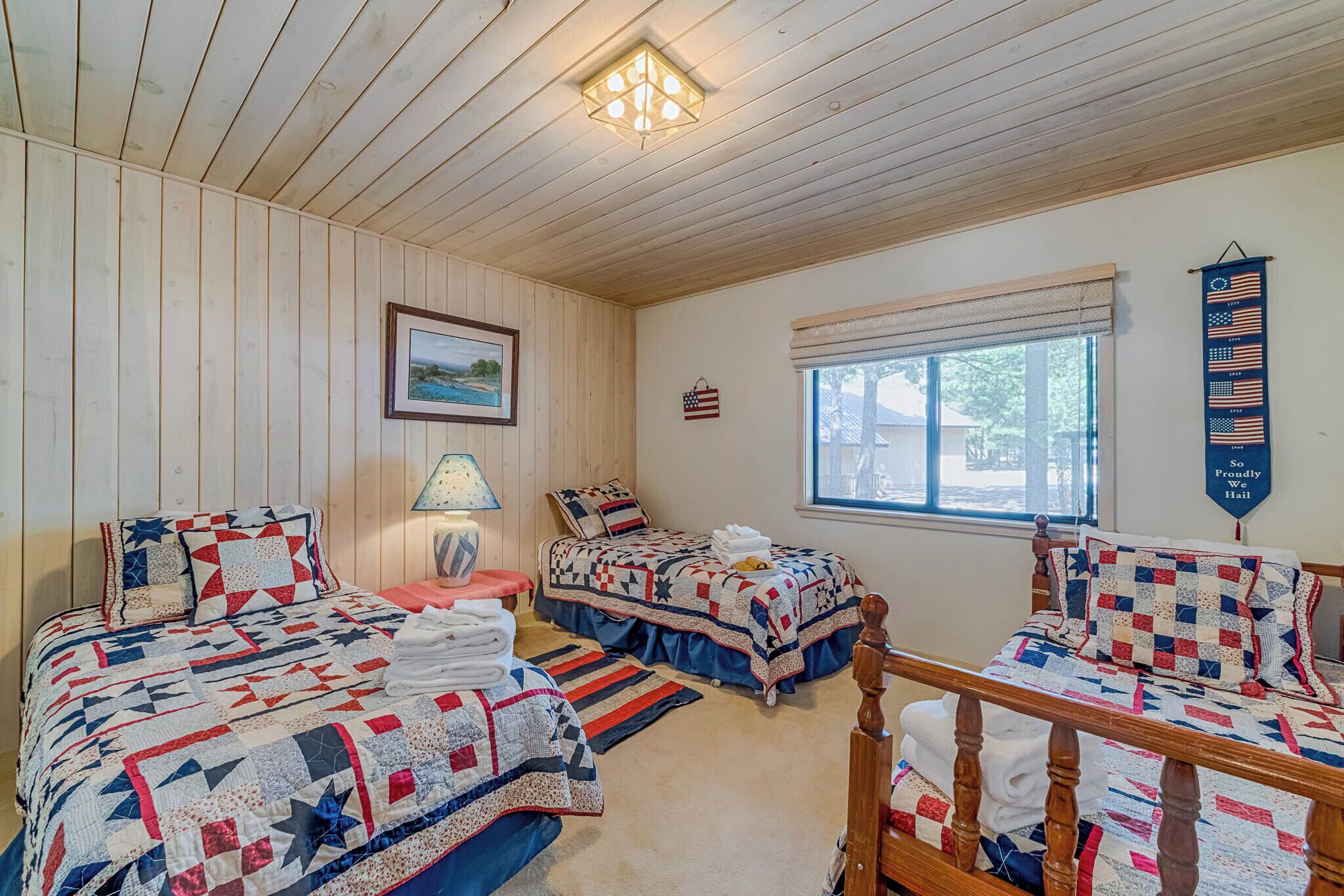 A bedroom with two beds, a wooden ceiling, a window with a view, and a wall with a flag and a sign.