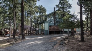 Un chalet doté d’une grande terrasse et d’un espace abrité, entouré de grands pins.