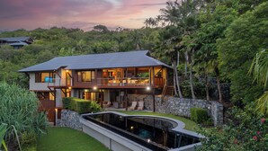 A modern two-story house with a swimming pool, surrounded by lush greenery and palm trees. - Iluka Luxury House With Ocean Views On Half Acre With Pool And Two Golf Buggies (Whitsundays)