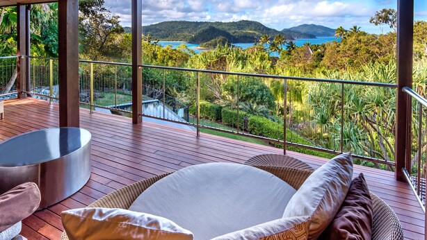 A wooden deck with a glass balustrade overlooking a lush landscape and a body of water. - Iluka Luxury House With Ocean Views On Half Acre With Pool And Two Golf Buggies (Whitsundays)