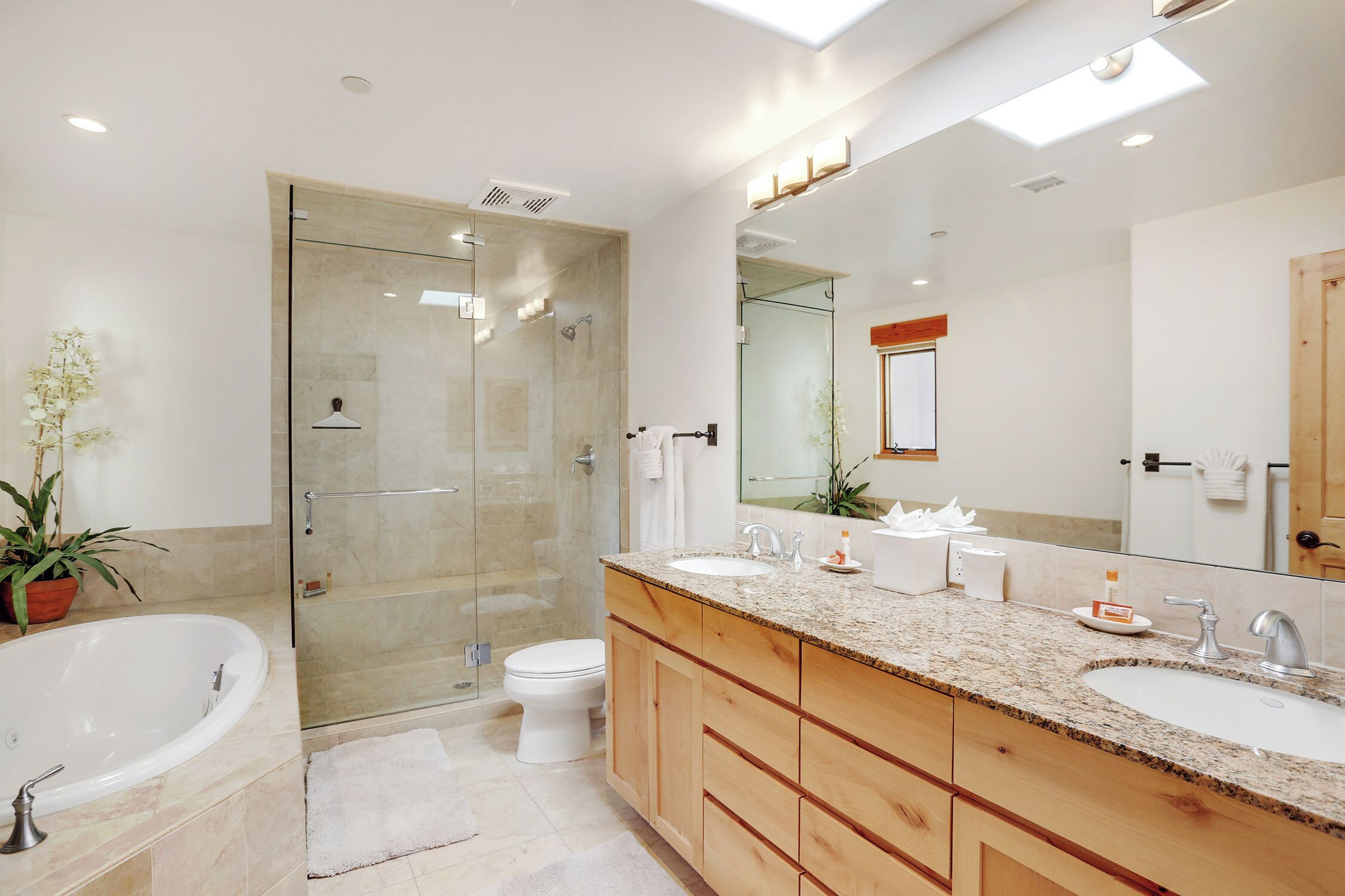 A modern bathroom with a glass-enclosed shower, a freestanding bathtub, and a large vanity with a granite countertop.