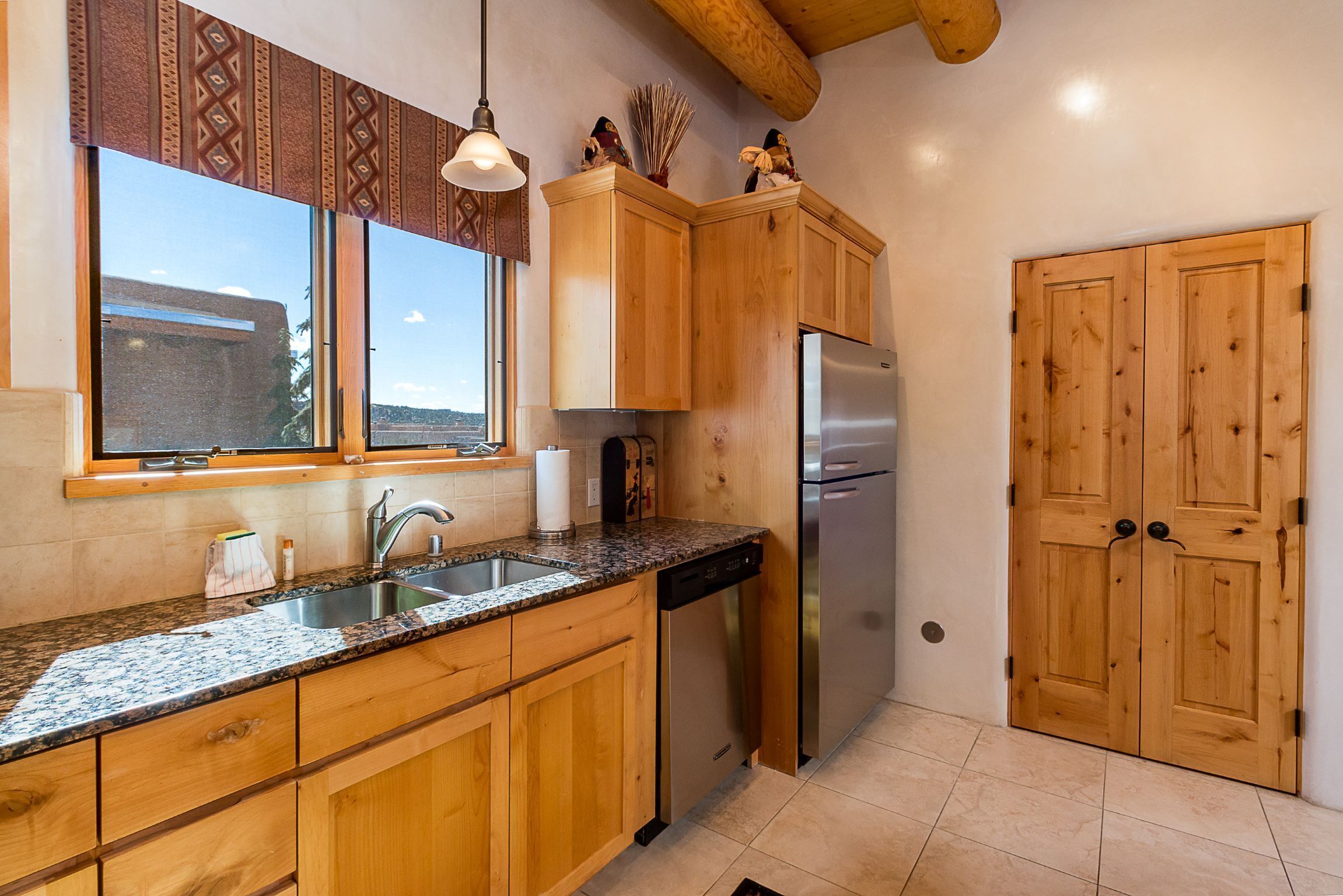 Una cocina con armarios de madera, un refrigerador de acero inoxidable, una encimera de granito y una ventana con cortinas estampadas.